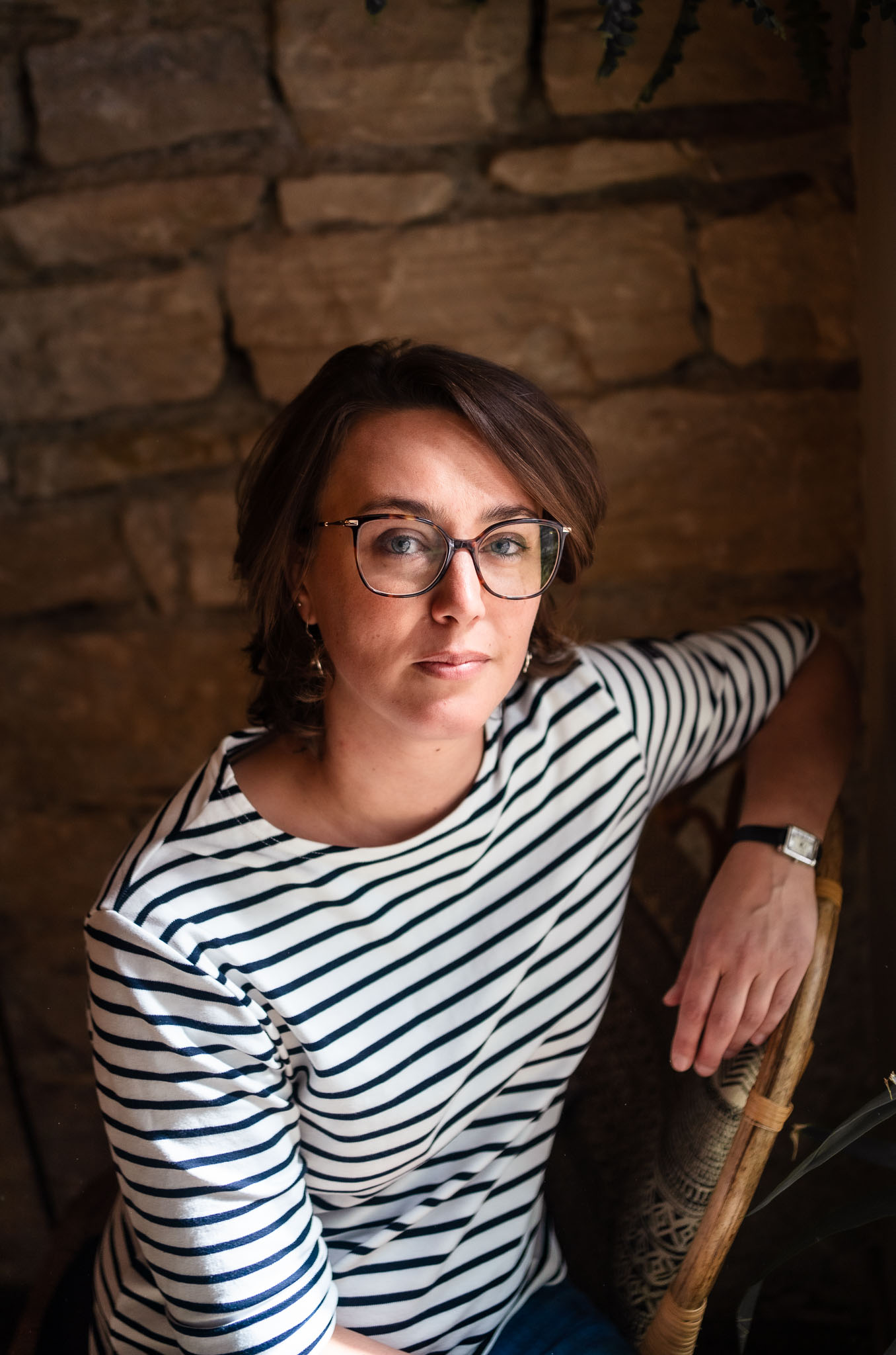 Portrait de Malvina Raynaud, consultante en communication digitale, assise dans un intérieur chaleureux, portant une marinière et des lunettes