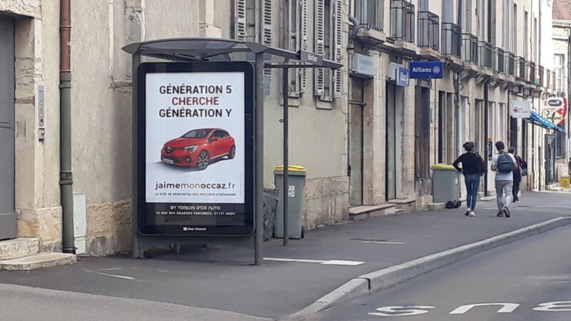 Panneau publicitaire en bord de rue pour un site de voitures d'occasion, mettant en avant la recherche de véhicules de génération 5 et Y